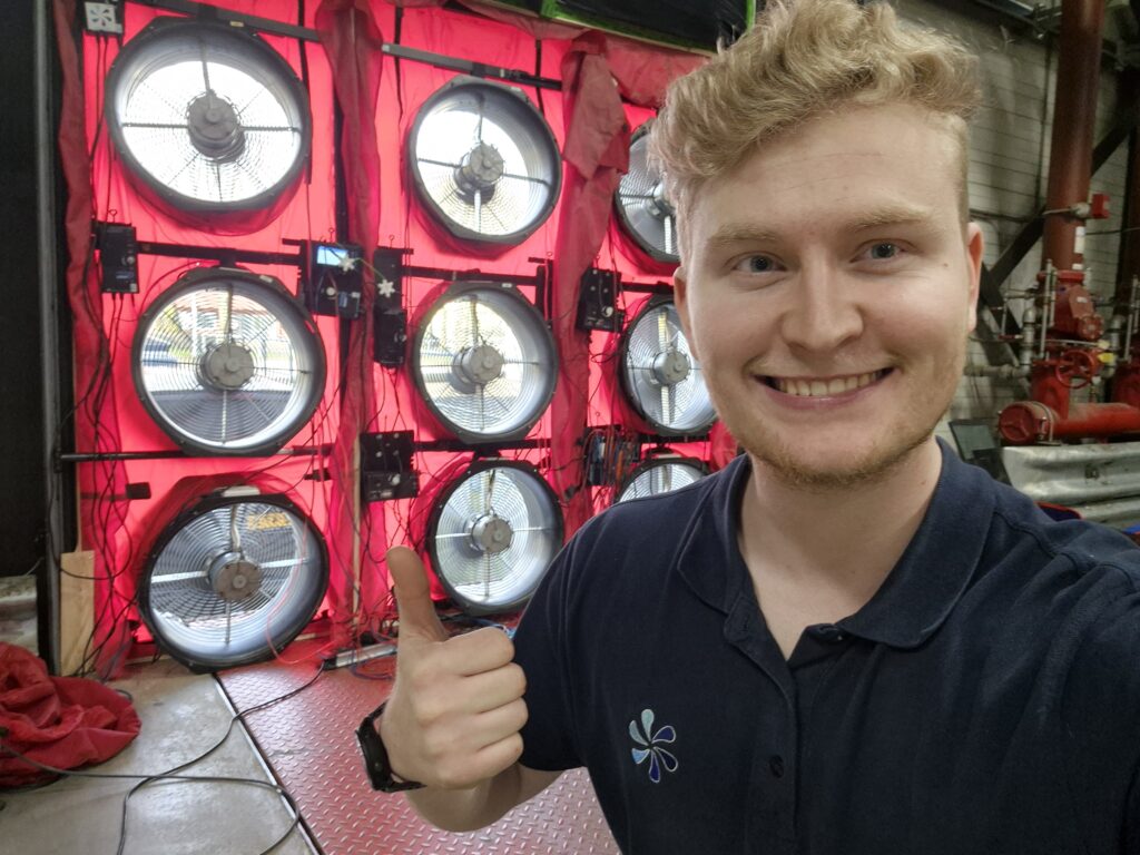 Technicus maakt een selfie bij een blowerdoor testopstelling met meerdere ventilatoren, gebruikt voor luchtdichtheidsmetingen in een gebouw.