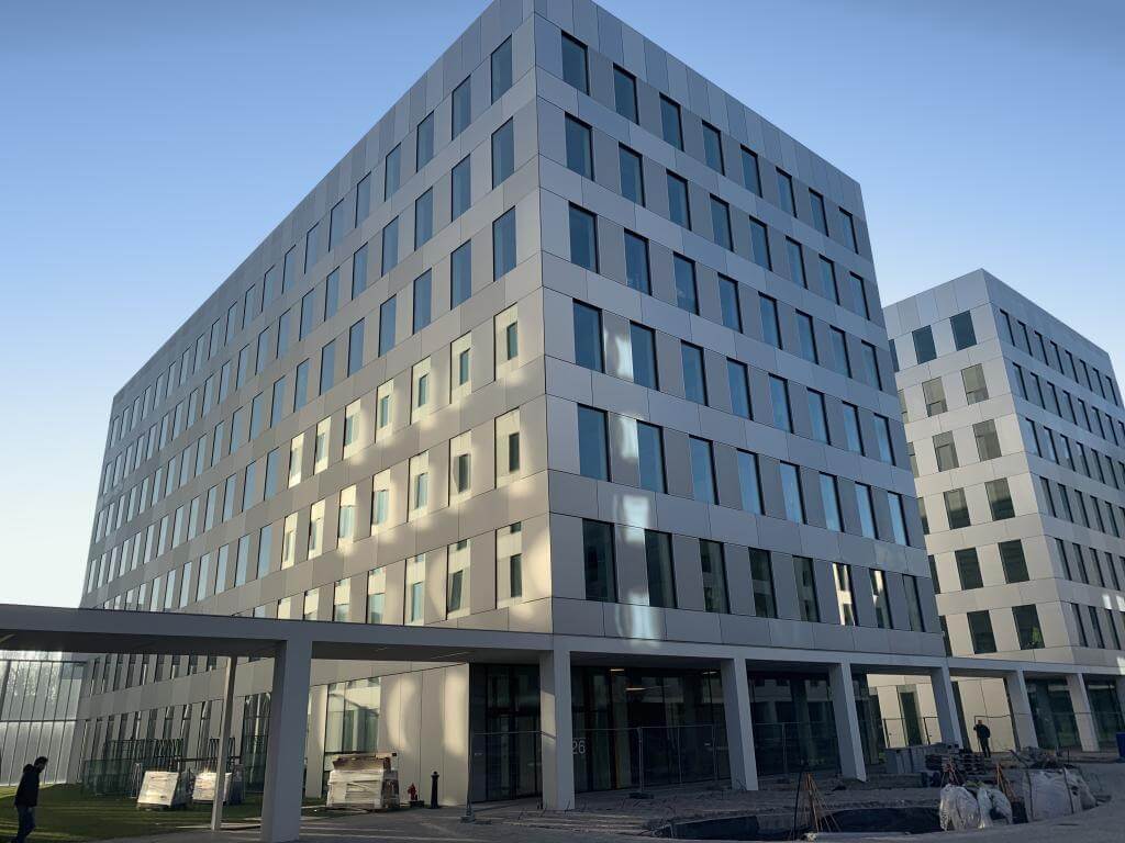Modern kantoorgebouw met meerdere verdiepingen en strakke gevel, gefotografeerd tijdens de bouwfase met bouwmaterialen en werkzaamheden zichtbaar op de voorgrond.