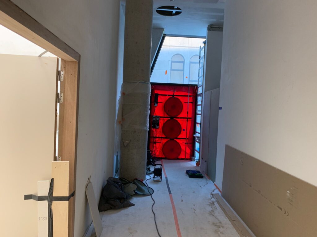 Blowerdoor testopstelling met drie ventilatoren in een deuropening aan het einde van een gang in een gebouw in aanbouw, gebruikt voor luchtdichtheidsmetingen.