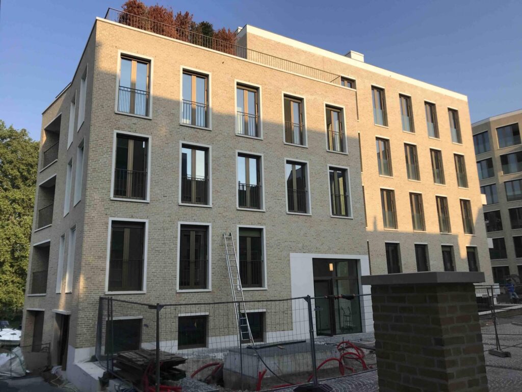 Nieuwbouw appartementencomplex met bakstenen gevel en meerdere verdiepingen, gefotografeerd tijdens de afbouwfase met bouwhekken en materialen op de voorgrond.