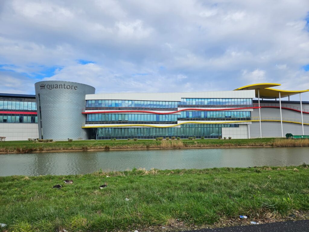 Modern bedrijfsgebouw van Quantore met glazen gevel en kleurrijke lijnen, gelegen aan het water in een groene omgeving.