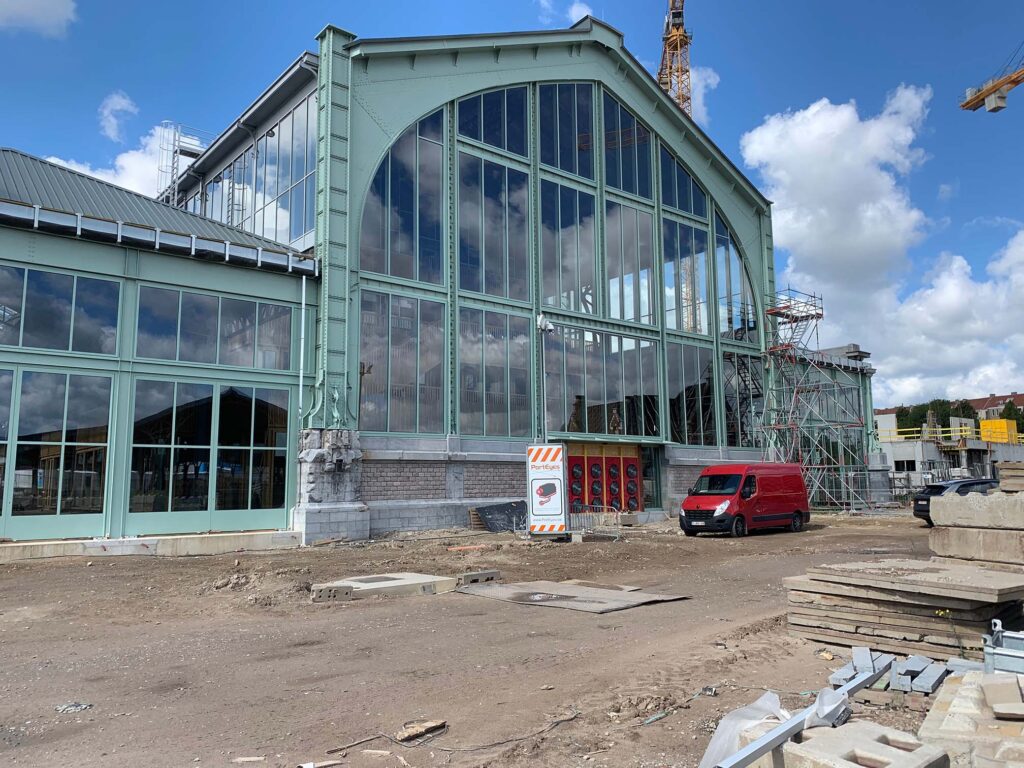 Groot industrieel gebouw met glazen gevel in renovatie, met blowerdoor testopstelling zichtbaar en bouwactiviteiten rondom het pand.