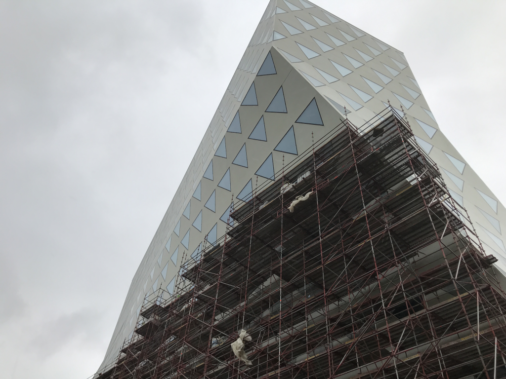 Modern, geometrisch vormgegeven gebouw met driehoekige ramen, gefotografeerd tijdens de bouwfase met steigers rondom de gevel.