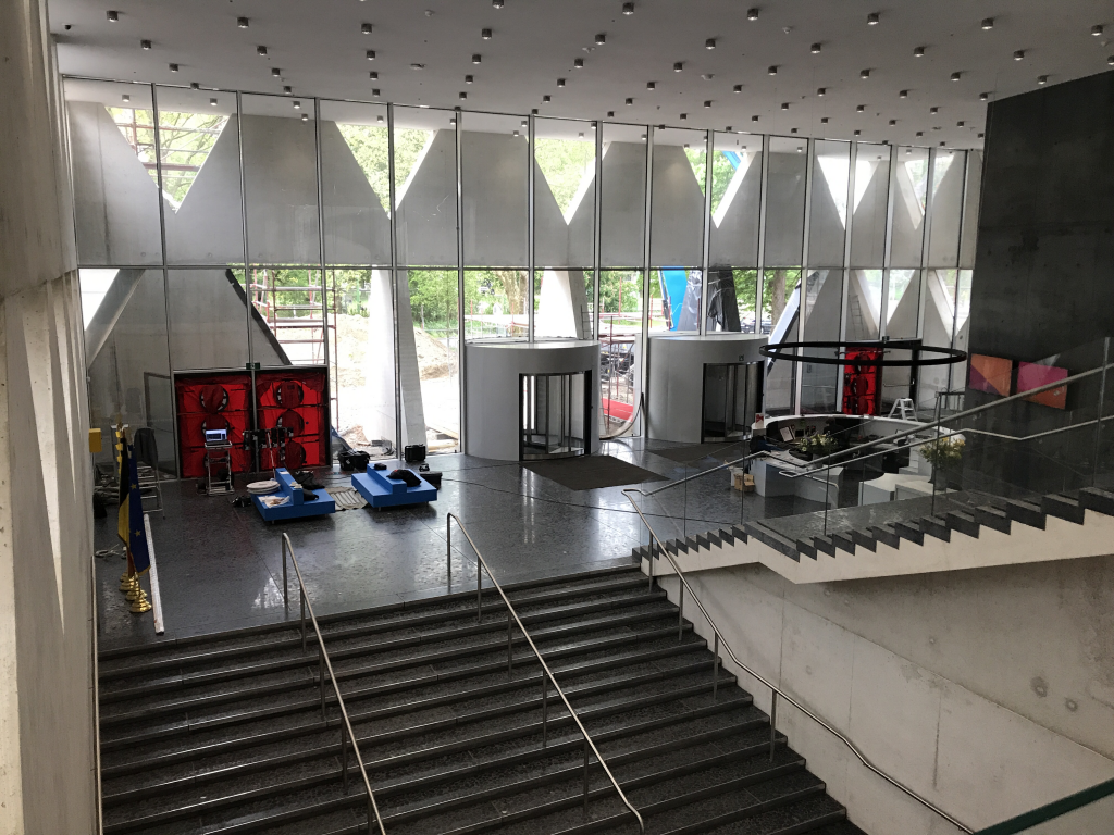 Grote entreehal met hoge glazen gevel en meerdere blowerdoor testopstellingen, ingericht voor luchtdichtheidsmetingen in een modern gebouw.