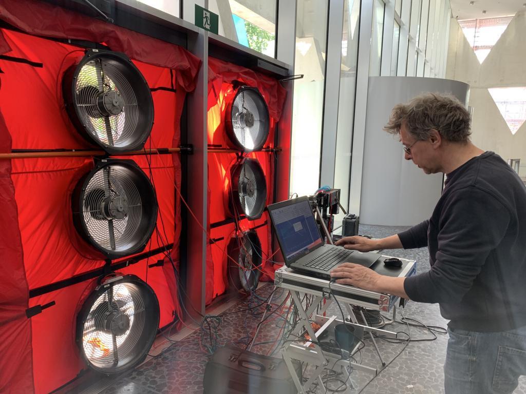 Technicus voert een blowerdoor test uit met meerdere ventilatoren in een deuropening, terwijl meetapparatuur en laptop worden gebruikt voor luchtdichtheidsmetingen.