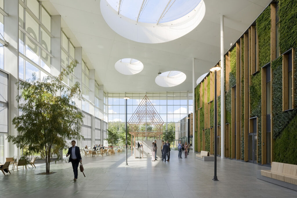 Ruime, moderne entreehal van het Liander-kantoor met grote glaspartijen, groene wand en veel daglicht, ingericht als ontmoetings- en werkruimte.