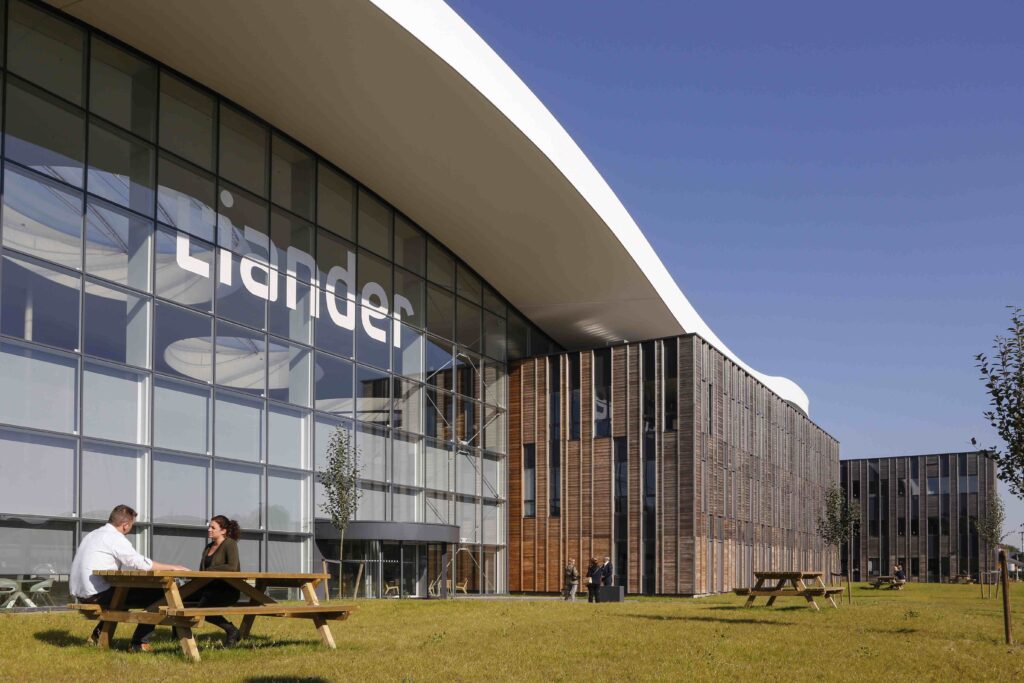 Modern kantoorgebouw van Liander met grote glazen gevel en houten bekleding, gelegen in een groene omgeving met zitplaatsen buiten.