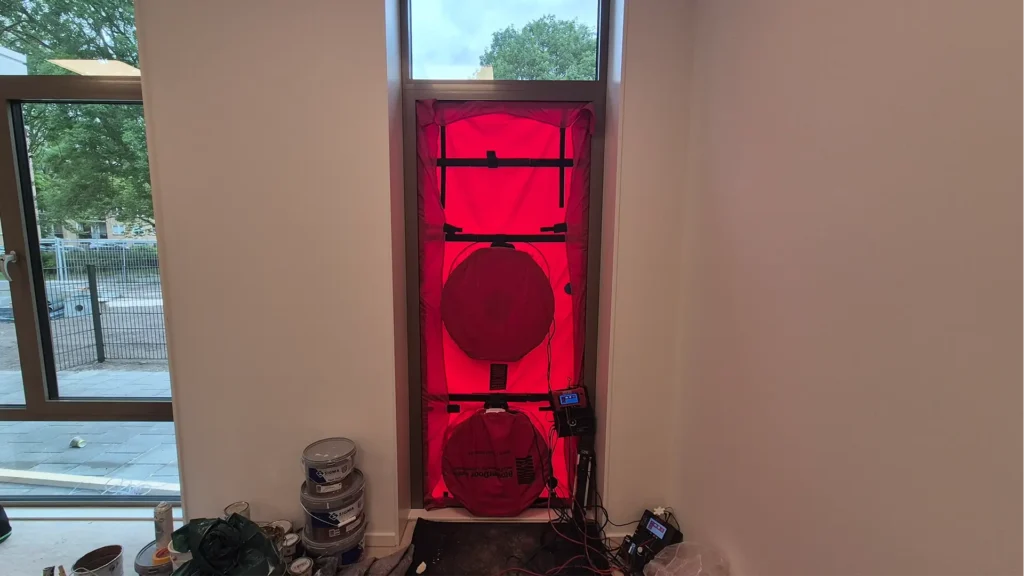 Blowerdoor testopstelling met ventilatoren en meetapparatuur in een deuropening, geplaatst in een ruimte tijdens de afbouwfase voor luchtdichtheidsmeting.
