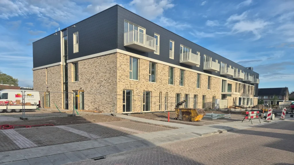 Modern nieuwbouwcomplex met bakstenen gevel en balkons, waarbij de buitenruimte en infrastructuur nog in aanleg zijn.