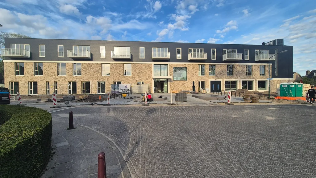 Nieuwbouw woon- of zorgcomplex met moderne bakstenen gevel en balkons, waarbij de buitenruimte en bestrating nog in aanleg zijn.
